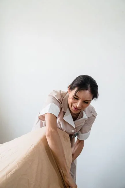 home-img Employée de ménage souriante disposant des coussins sur un canapé dans un salon lumineux.